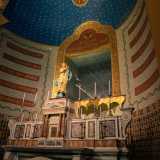 ...sovrastato dalla statua in cartapesta dell�Immacolata. La sottostante parete curvilinea � caratterizzata dalla sovrapposizione di un basamento con marmi policromi, una fascia con colorati motivi geometrici, un registro superiore con fasce di testi liturgici dorati...